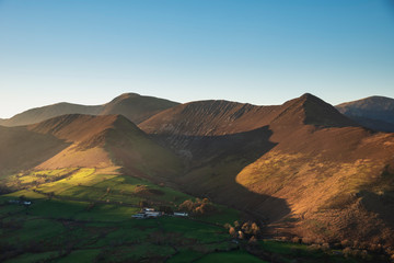 Beautiful Autumn Fall landscape image of sun beams lighting up small area of mountain side in Lake District whilst rest of area is in darkness with Robinson and Dale Head in background