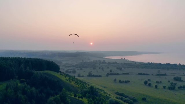 Green trees at sunset with a sailwing flying above them. Paraglider in the sky.