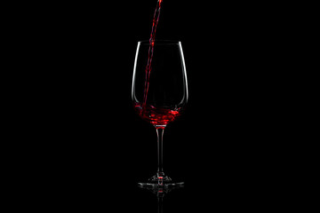 Red wine pouring into a wine glass, over black background, horizontal image