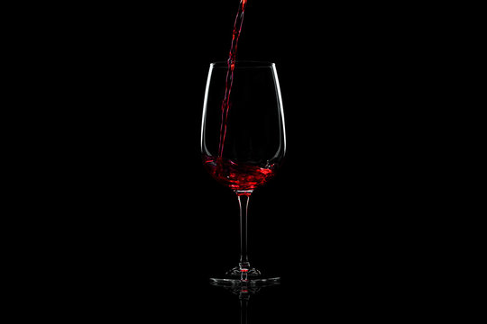 Red wine pouring into a wine glass, over black background, horizontal image