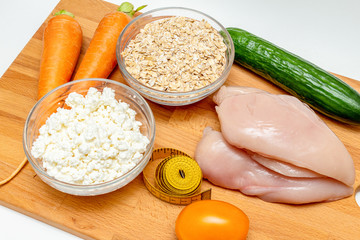 raw chicken breast, cereals, measuring tape, farm cottage cheese carrot vegetables close up on wooden background protein healthy diet fat free concept eco product sports nutrition
