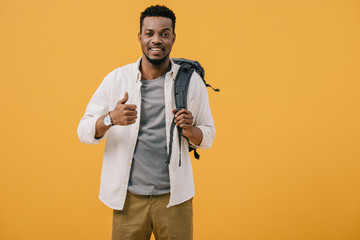 happy african american man showing thumb up and touching backpack isolated on orange