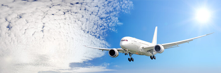 modern airplane flying against blue sky with clouds and sun background aerial front utra wide panorama view of passenger plane landing with aircraft gear parts extended air travel aviation concept