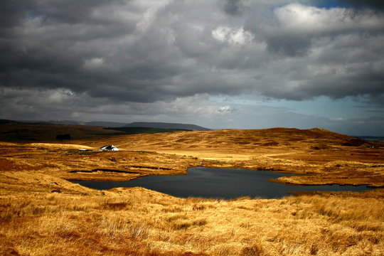 Moody landscape from Connemara, Ireland with golden fields, dark ominous lake and stormy clouds over the mountains