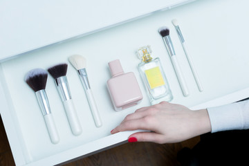 The woman opens shelf, face cream jars, set of makeup brushes, perfume, woman's hand, close up, white background, copy space, for text, top view