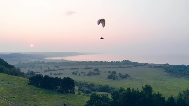 A person on a parawing is gliding above the green landscape