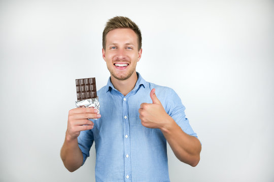 Young Handsome Man Holding Chocolate Bar Showing Like Sign Smiling On Isolated White Background