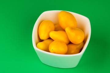 Yellow tomatoes in bowl on green background