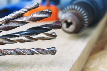 Drills near power drill on a wooden background. The concept of tools and repair work.