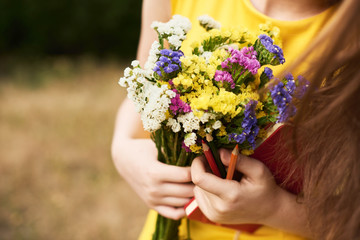 long-haired blond girl standing in the park with flowers, a notebook and pencils in her hands. Ready to school. Back to school