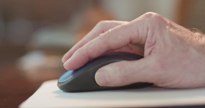 The hand of a Caucasian male using a wireless computer mouse clicking and scrolling actions to whatever work he is doing off screen.