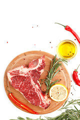 Raw t-bone steak on a wooden board with rosemary and spices on a white background. Top view.