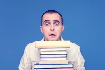 Frightened young man with books, open his mouth, close up, the concept of heavy loads in education