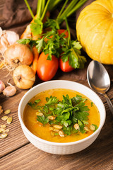 Pumpkin and fresh vegetables soup in white bowl wooden background. Natural rustic style. Vertical frame. Autumn concept.