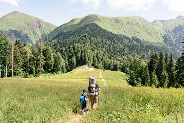 Dad and son go to the mountains along the trail, hiking with backpacks. The concept of parenting, joint family time, a healthy sports lifestyle.