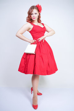 Beautiful redheaded girl in red midi pinup style dress isolated on white studio background standing alone
