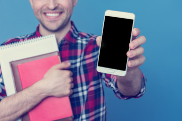 Happy student with books, shows the screen of the smartphone, portrait, blue background, copy space