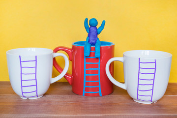 Success concept, plasticine man sitting on a mug with drawn ladder.