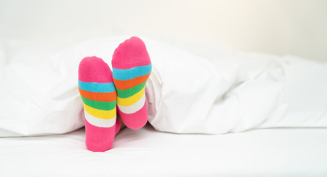 Female foot in warm stripe wool sock ,Woman sleeping and relaxing in bed concept. Warm and cozy white socks in the bed