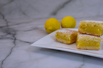 Close view of home baked lemon squares, lemon bars over white plate and marbled background 