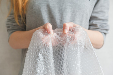 Female hands popping the bubbles in bubble wrap. Selective focus, close up.