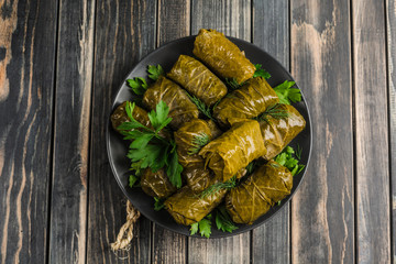 Delicious stuffed grape leaves (traditional doom Mediterranean cuisine Dolma) on a black plate with fresh cilantro and dill