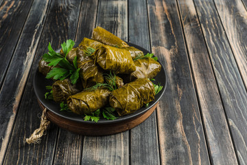 Delicious stuffed grape leaves (traditional doom Mediterranean cuisine Dolma) on a black plate with fresh cilantro and dill