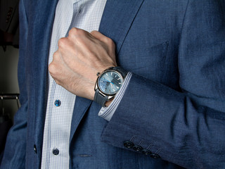 A man in a classic suit shows an expensive wristwatch