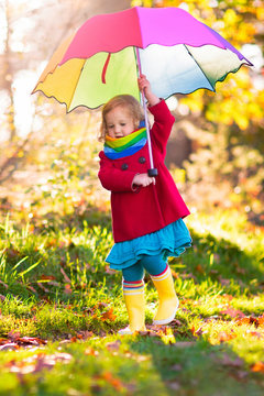 Kid with umbrella playing in autumn rain.