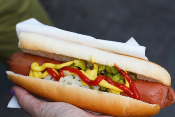 Hot-dog sausage with ketchup mustard and pickled cucumbers and onions in a female woman hand,  street food quick, top view
