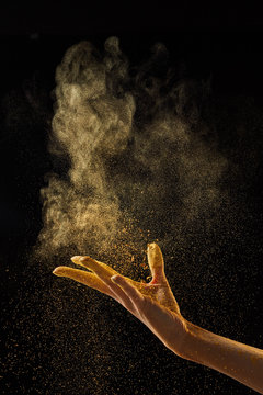 Woman's hand scatters gold dust on a black background with copy space. Creative photo for your ideas