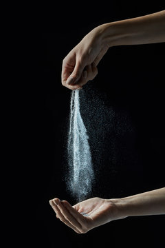 Woman's hand pours silver dust into her palm around a black background with copy space.