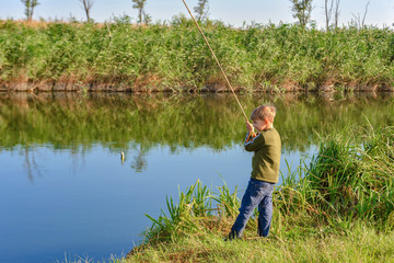 A fishing boy on a river holds a fishing rod, a child caught a fish and pulls it out of the water...