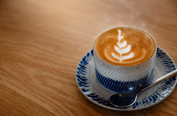 Drinking cup of coffee during day helps to refresh and relax. A  beautiful leaf-shaped latte art on wooden floors and space in the coffee shop. Caffeine makes people alert and increases energy levels.