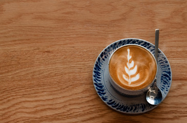 Top view Drinking cup of coffee during day helps to refresh and relax. Beautiful leaf-shap latte art on wooden floors and space in coffee shop. Caffeine makes people alert and increases energy levels.