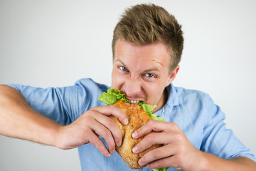 young handsome hungry man biting fresh sandwich with salad leaf on isolated white background