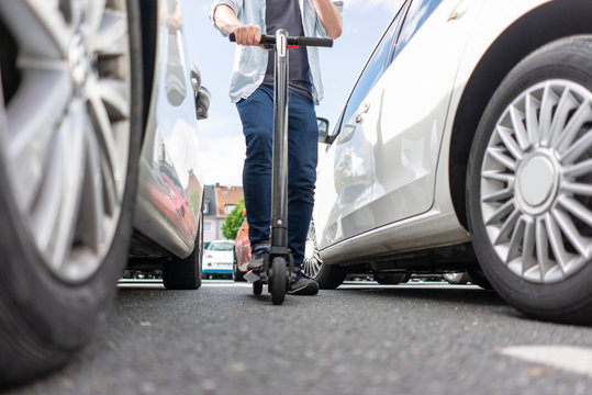 Man with E-Scooter between two cars, partial view