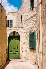 Narrow street leading to a green wooden door belonging to a house, Ghajnsielem, Gozo, Malta