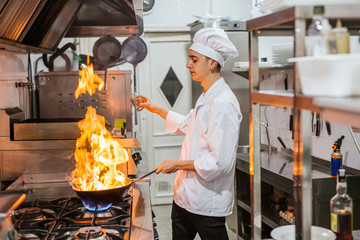 Junior chef with pan of flames in traditional spanish restaurant kitchen