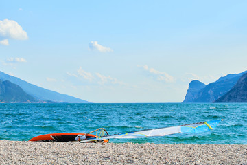 Windsurfing board lying on an empty pebble beach by the lake Garda (Lago di Garda), Italy