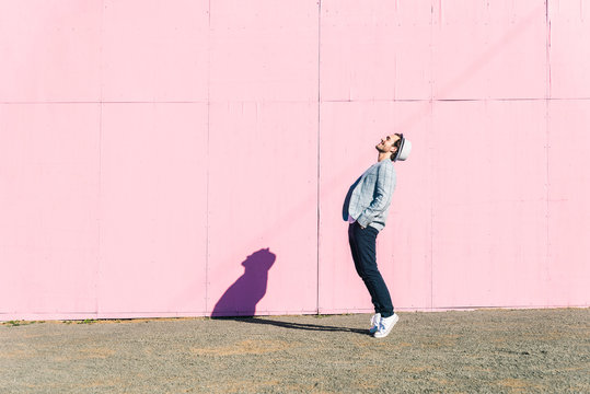 Happy young man in front of pink construction barrier, standing on tiptoes, smiling