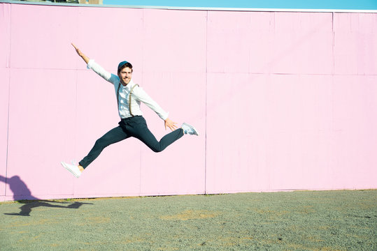Young man in front of pink construction barrier, jumping in the air