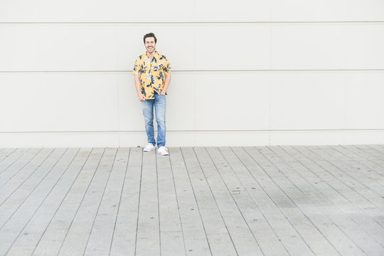 Happy young man wearing aloha shirt, standing against house wall