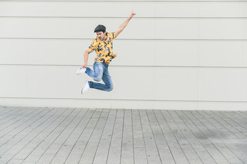 Young man wearing flat hat and aloha shirt, jumping for joy