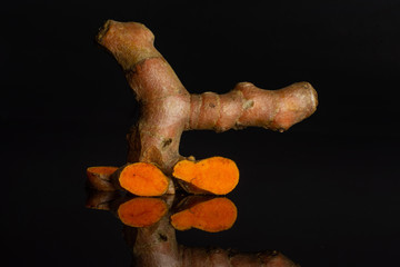 Group of one whole three slices of bright turmeric rhizome isolated on black glass