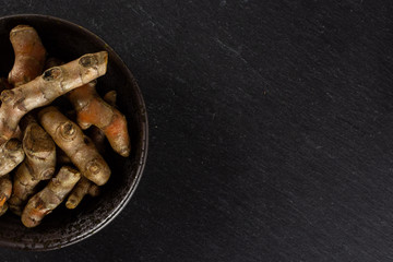 Lot of whole bright turmeric rhizome copyspace on right on grey ceramic plate flatlay on grey stone