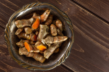 Lot of whole lot of slices of bright turmeric rhizome in old iron bowl flatlay on brown wood