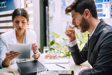 Two office workers discussing data in touchpad at meeting