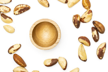 Lot of whole shelled brazil nuts near wooden bowl flatlay isolated on white background