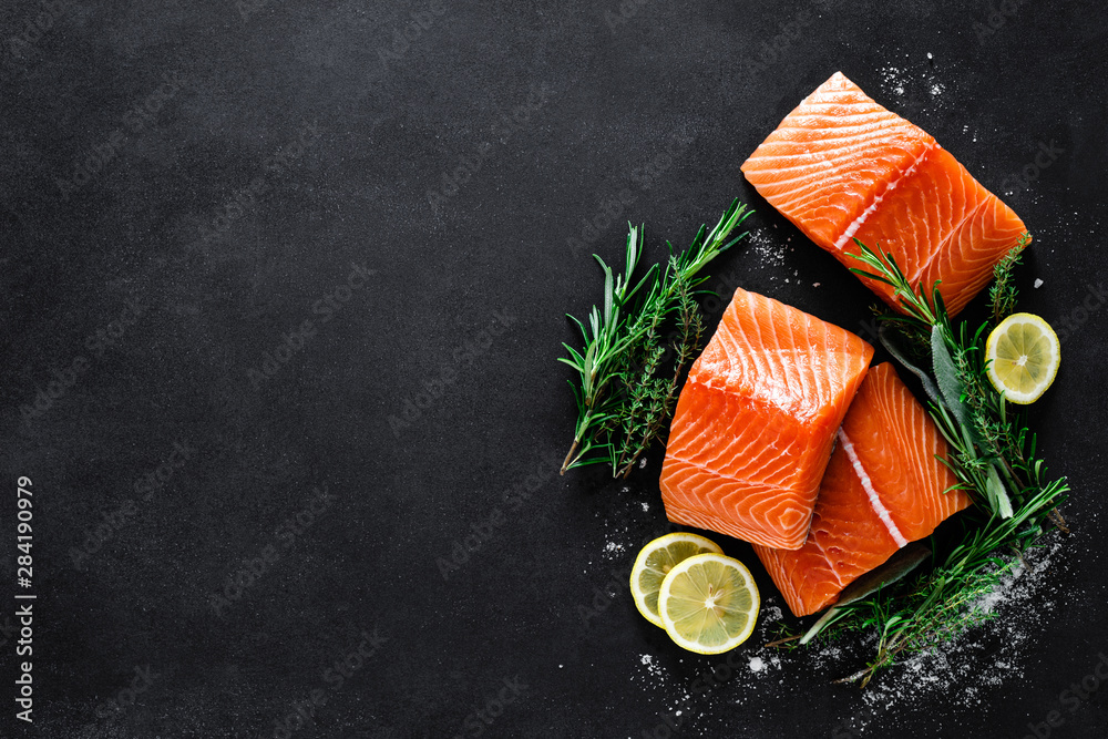 Wall mural salmon. fresh raw salmon fish fillet with cooking ingredients, herbs and lemon on black background, 